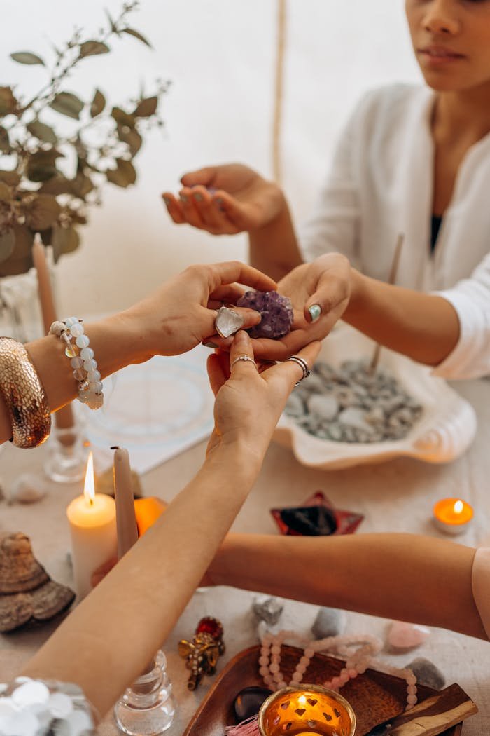 Hands exchanging amethyst crystals in a warm, candlelit spiritual setting.