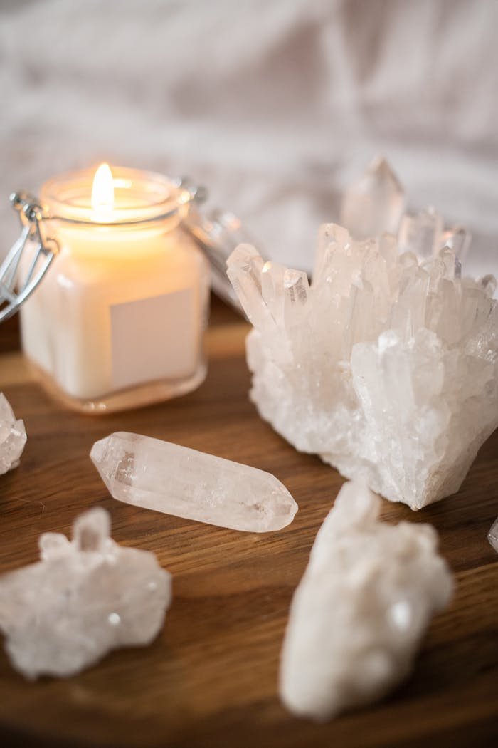 A burning candle surrounded by clear quartz crystals on a wooden tray, creating a peaceful ambiance.